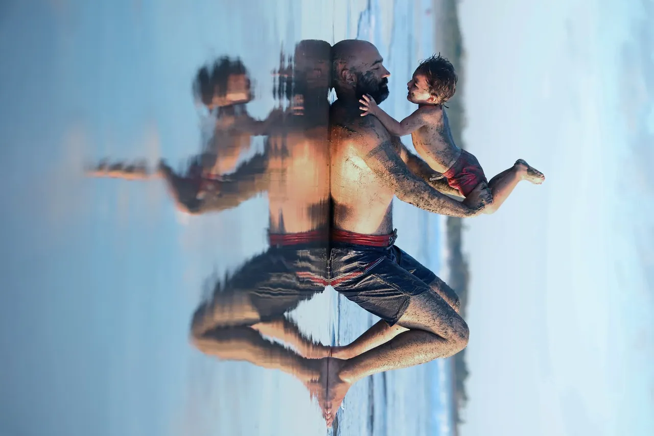 Papá con su bebé en la playa, reflejados en el agua